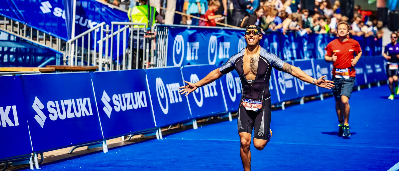 Bruno at a World Triathlon finish line with arms spread wide, crowds cheering