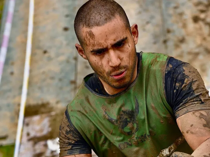 Bruno climbing a muddy rope obstacle during an ultra obstacle course race